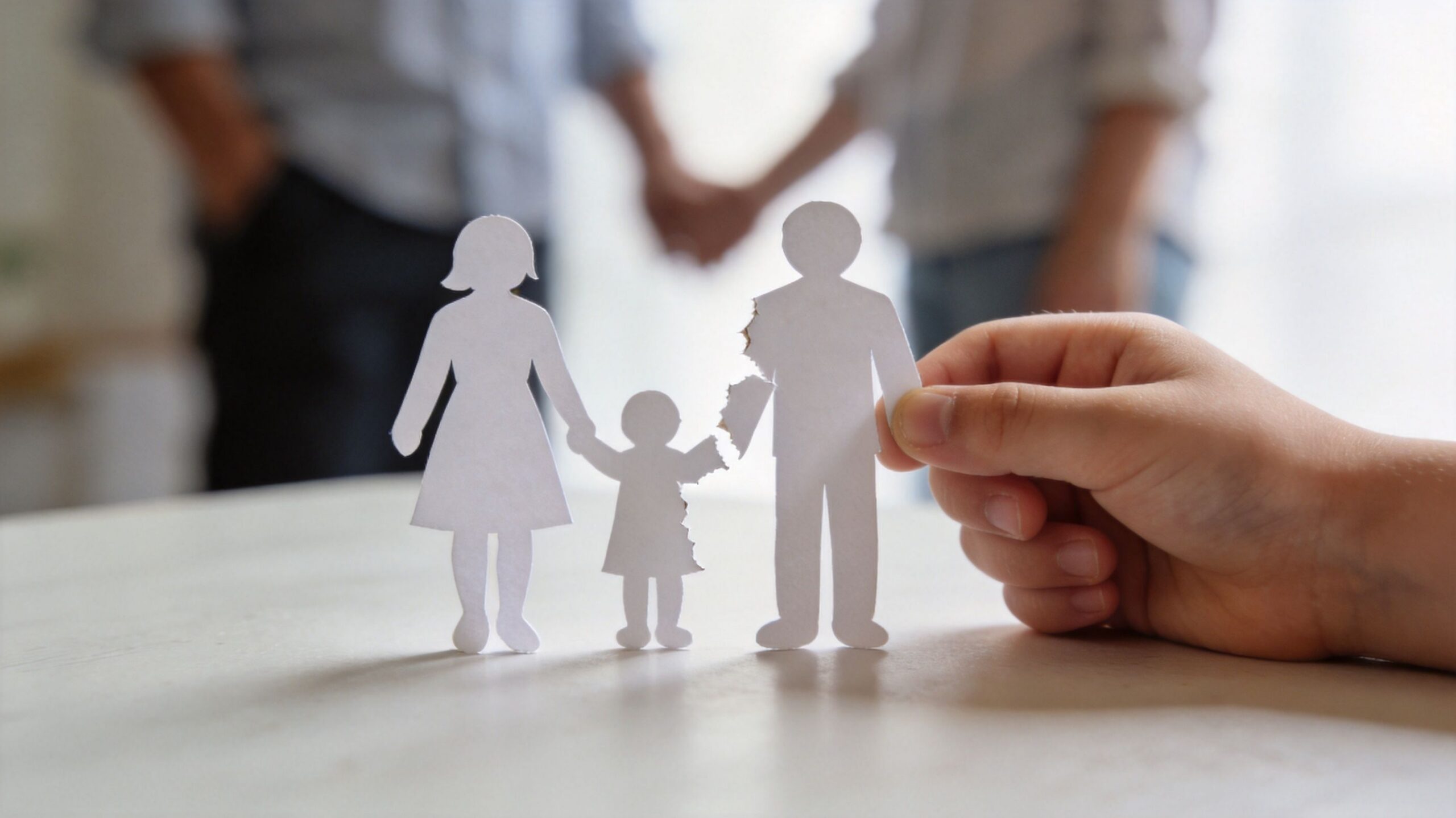 A child's hand holding a torn paper cutout of a family representing divorce and separation.